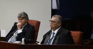 Luiz Fux e Flávio Dino sérios, sentados lado a lado, sem olhar para a câmera