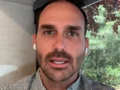 O deputado federal Eduardo Bolsonaro (PL-SP) em close, sério, falando para a câmera, usando fones de ouvido brancos sem fio