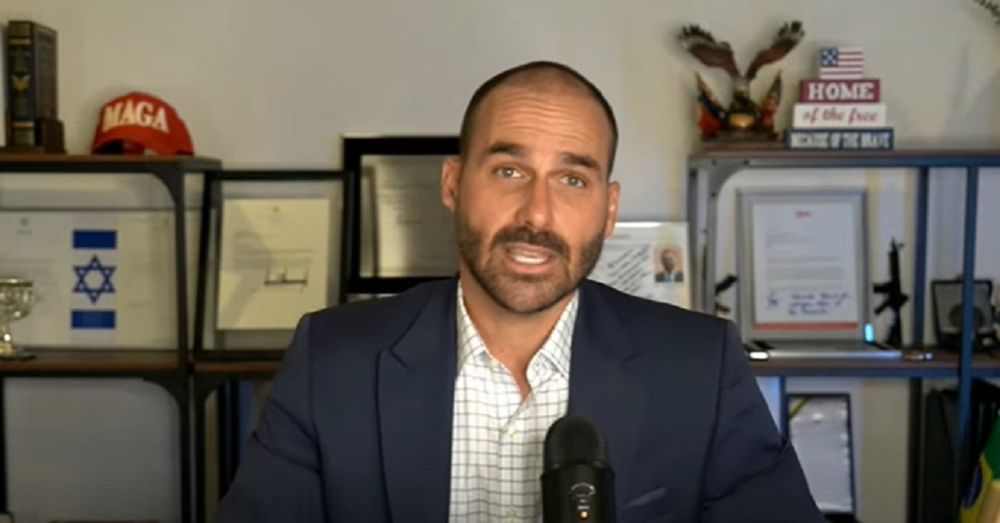 O deputado federal Eduardo Bolsonaro (PL-SP) falando para a câmera, sério, de roupa formal azul e branca