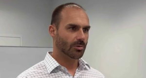 Eduardo Bolsonaro falando, sério, de camisa polo clara e quadriculada, sem olhar para a câmera