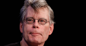 Stephen King em close, sério, de óculos