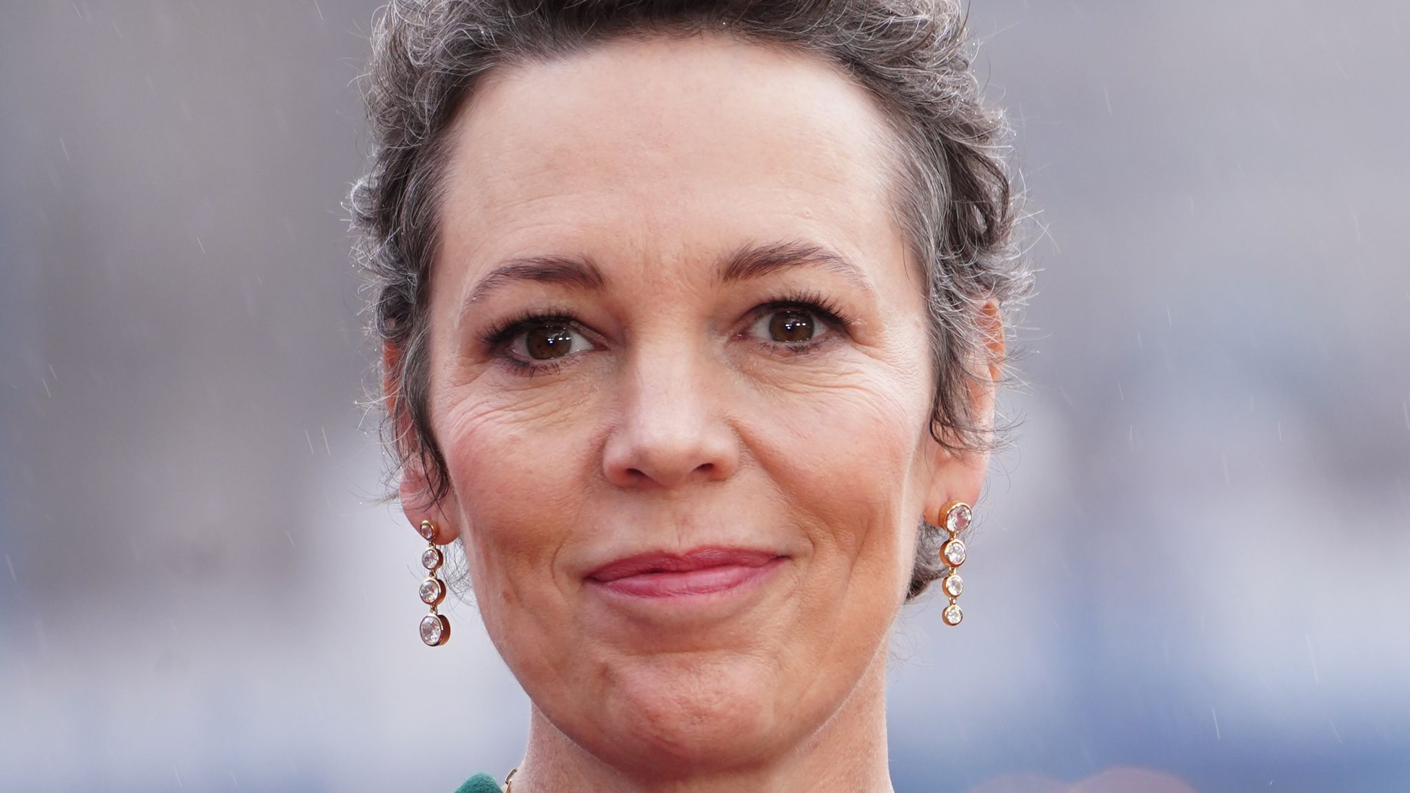 Olivia Colman em close, com sorriso tímido, olhando para a câmera