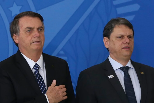 Jair Bolsonaro e Tarcísio de Freitas em pé, lado a lado, sérios, o primeiro com a mão no peito