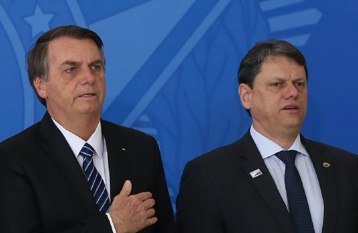 Jair Bolsonaro e Tarcísio de Freitas em pé, lado a lado, sérios, o primeiro com a mão no peito