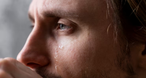 Homem loiro de olhos claros, em close, de perfil, chorando