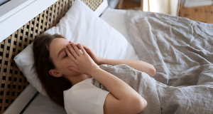 Mulher deitada na cama com as mãos no rosto