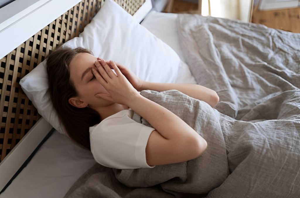 Mulher deitada na cama com as mãos no rosto