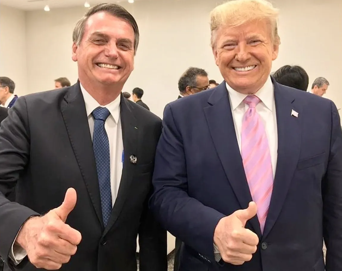 Jair Bolsonaro (PL) e Donald Trump sorrindo para foto e fazendo sinal de joia, ambos em pé, lado a lado