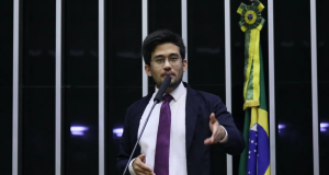 O deputado Kim Kataguiri (União-SP) em pé, falando em microfone e gesticulando, na Câmara dos Deputados