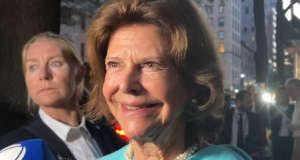 rainha Silvia da Suécia sorrindo sem olhar para a câmera, de roupa azul