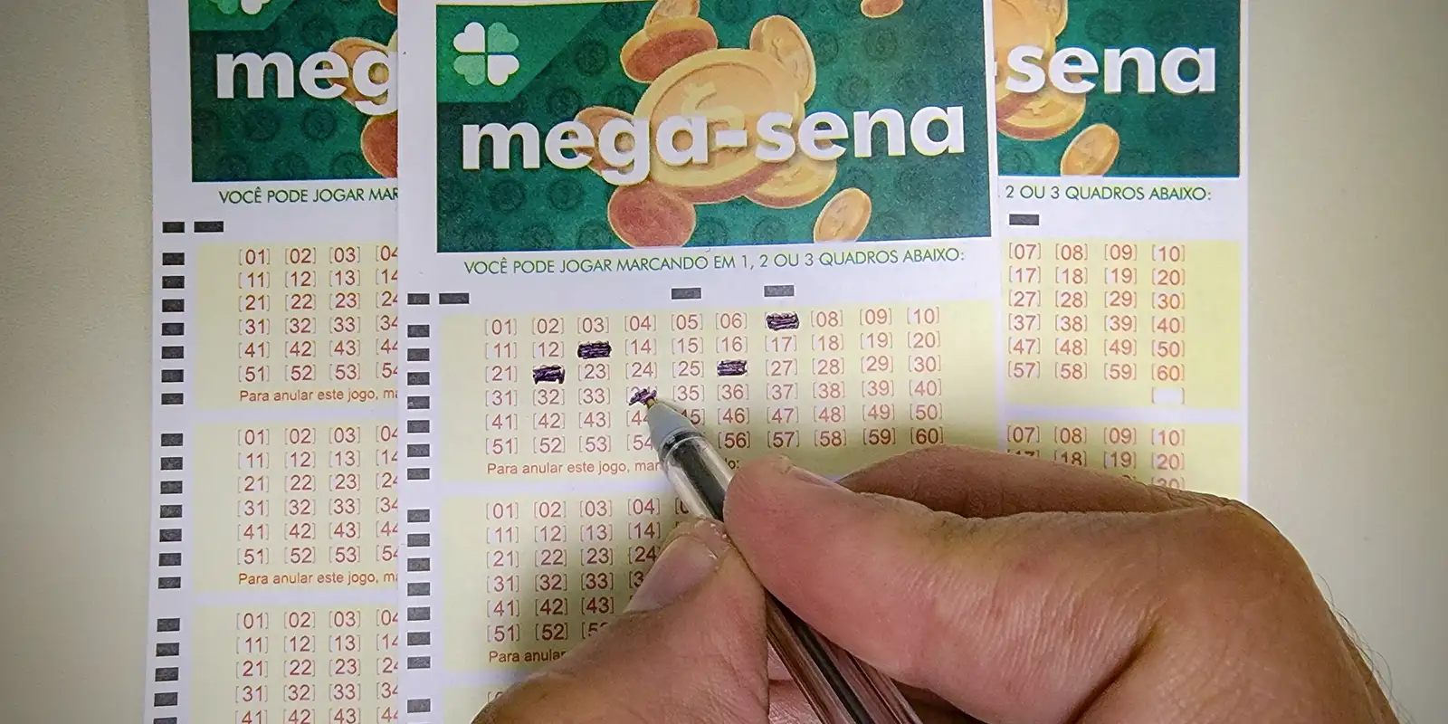 Mão segurando caneta e preenchendo talão da mega-sena