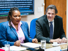 Margareth Menezes (Cultura) e Fernando Haddad (Economia) sentados lado a lado, ele sorrindo e ela séria