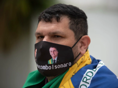 blogueiro bolsonarista Oswaldo Eustáquio de máscara, com bandeira do Brasil enrolada nos ombros