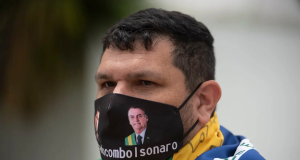 blogueiro bolsonarista Oswaldo Eustáquio de máscara, com bandeira do Brasil enrolada nos ombros