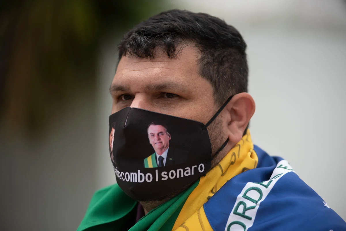blogueiro bolsonarista Oswaldo Eustáquio de máscara, com bandeira do Brasil enrolada nos ombros