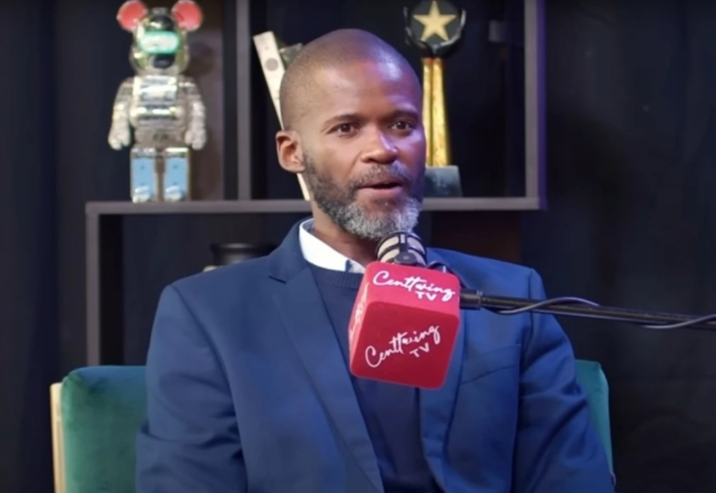 O pastor sul-africano Joshua Mhlakela falando em microfone, sério, sem olhar para a câmera