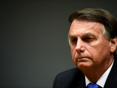 Jair Bolsonaro no canto direito de foto, em close, sério
