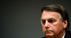 Jair Bolsonaro no canto direito de foto, em close, sério