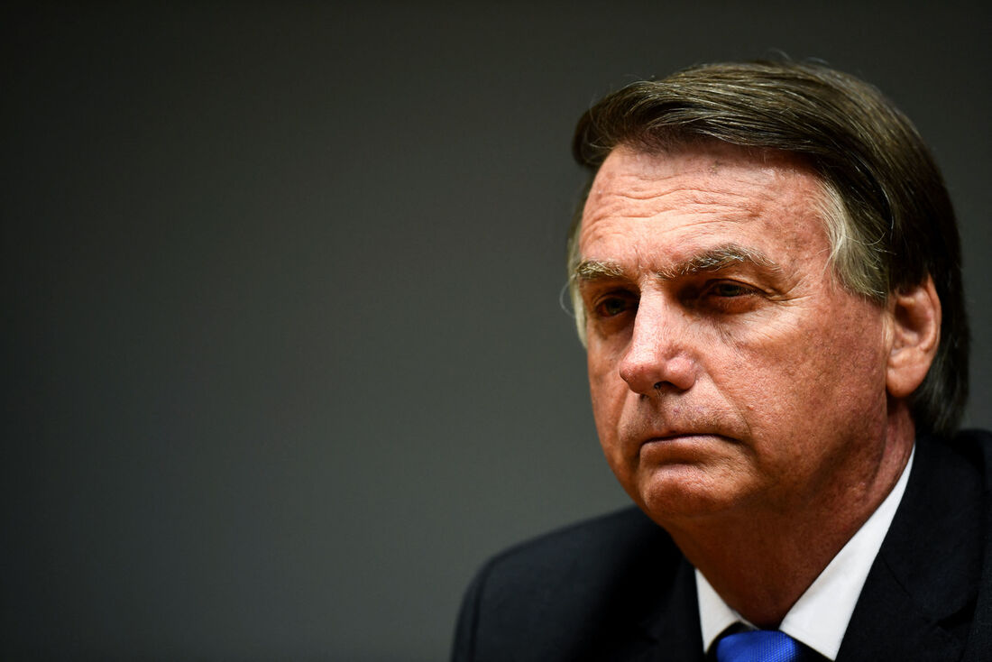 Jair Bolsonaro no canto direito de foto, em close, sério