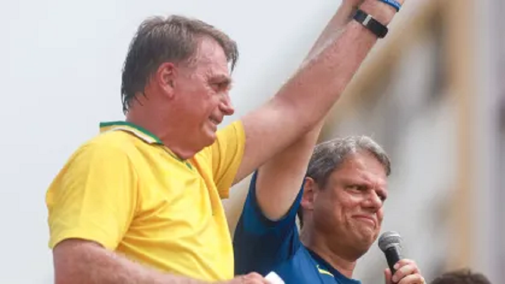 O ex-presidente Jair Bolsonaro (PL) e o governador de São Paulo, Tarcísio de Freitas (Republicanos), de mãos dadas e braços erguidos sorrindo sem olhar para a câmera