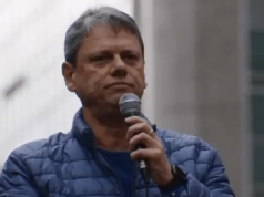 Tarcísio de Freitas de roupa de frio azul, sério, segurando microfone