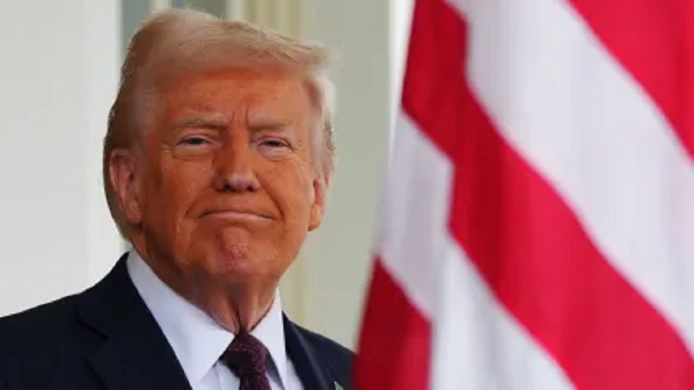 O presidente dos Estados Unidos, Donald Trump, em close, sorrindo de maneira debochada, com bandeira dos EUA ao fundo