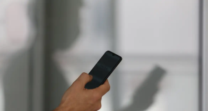 Mão mexendo no celular com sombra de homem ao fundo