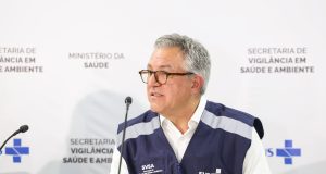 O ministro da Saúde, Alexandre Padilha, falando em microfone sem olhar para a câmera, de óculos