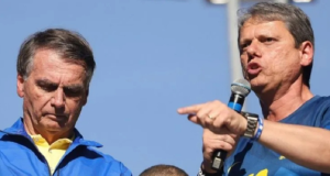 Jair Bolsonaro cabisbaixo e Tarcísio de Freitas falando em microfone