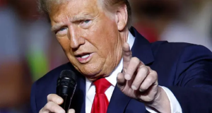 Donald Trump, presidente dos EUA, falando em microfone e apontando pra frente, em close
