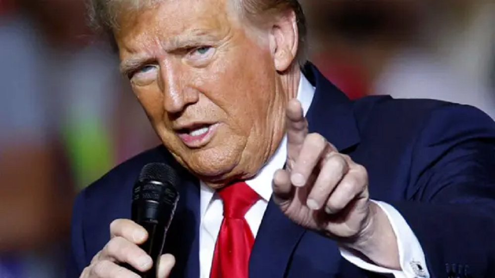 Donald Trump, presidente dos EUA, falando em microfone e apontando pra frente, em close