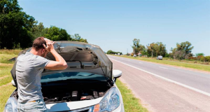Homem de costas, na estrada, com as mãos na cabeça, com o carro aberto