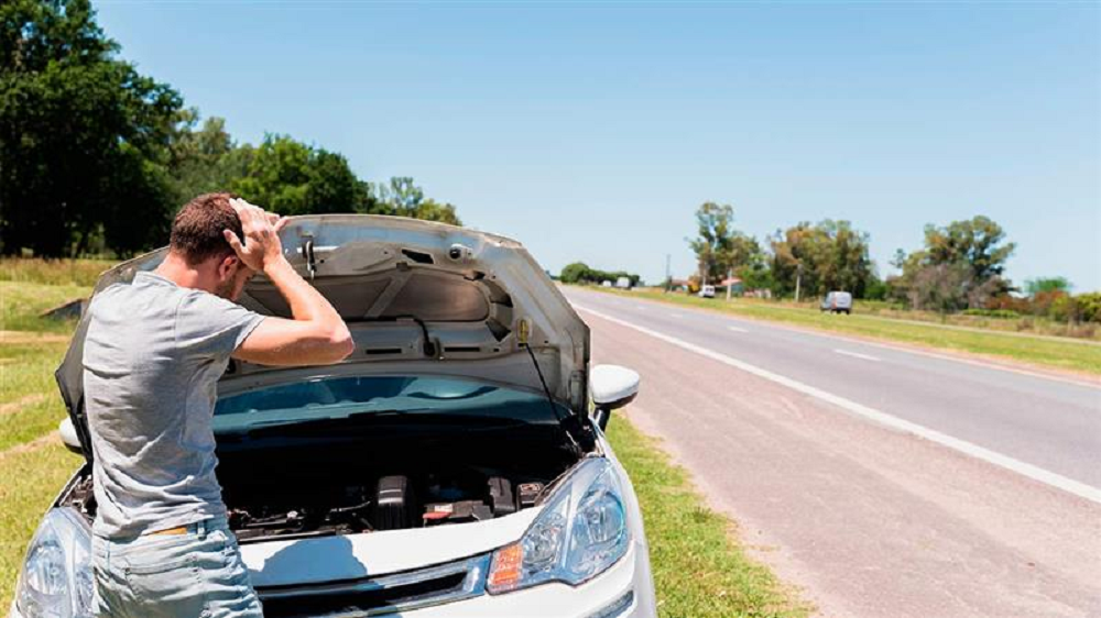 Homem de costas, na estrada, com as mãos na cabeça, com o carro aberto