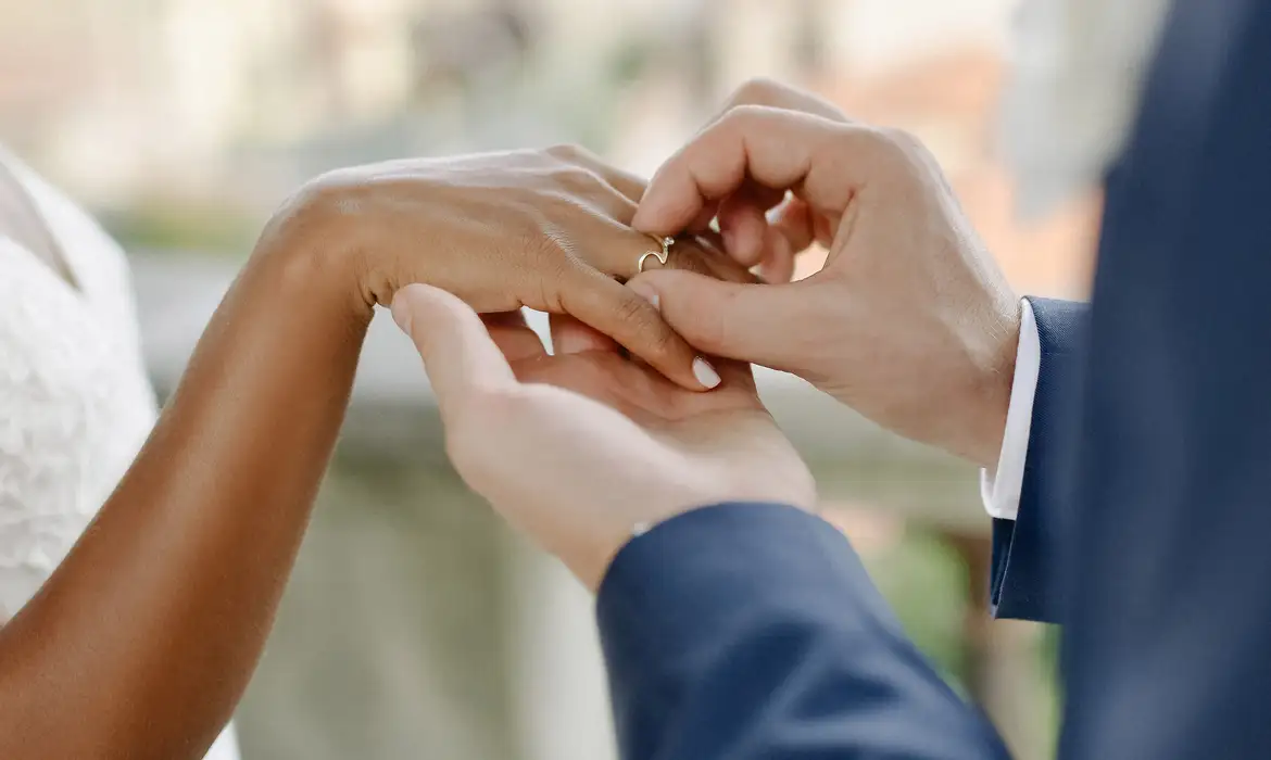 Mão masculina colocando aliança em mão feminina