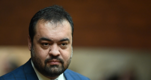 Claudio Castro sério, no canto esquerdo da foto, sem olhar para a câmera, de roupa social azul