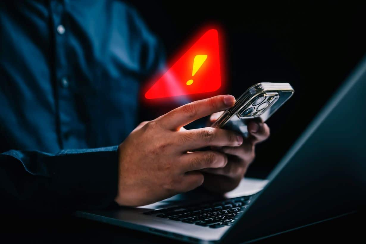 Mão mexendo em celular com sinal de alerta em arte