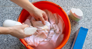 Peça de roupa branca em bacia, mãos esfregando com água