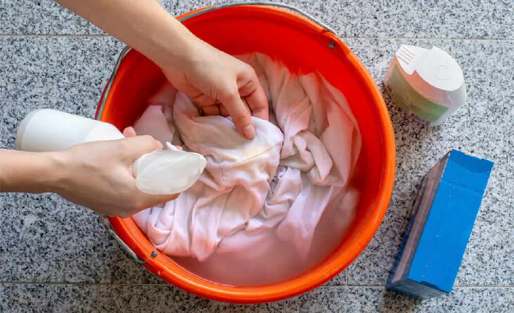 Peça de roupa branca em bacia, mãos esfregando com água