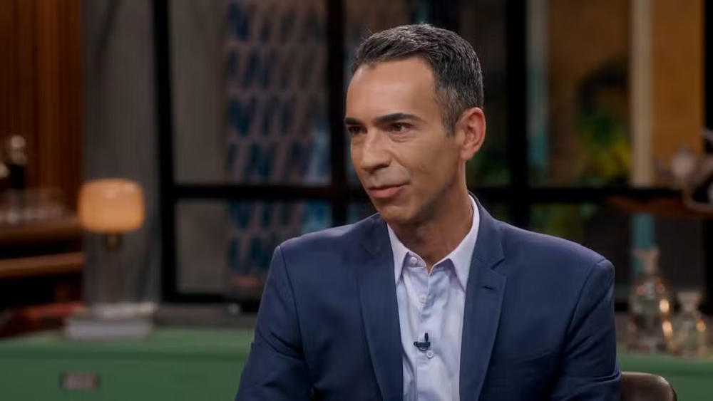César Tralli no Conversa com Bial, de roupa social azul marinho, falando sem olhar para a câmera