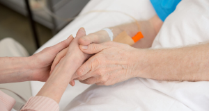 Duas pessoas de mãos dadas em leito de hospital