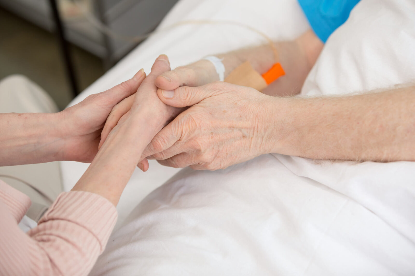 Duas pessoas de mãos dadas em leito de hospital