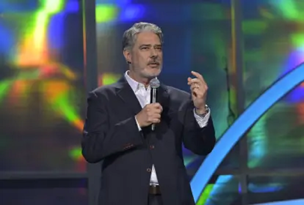 William Bonner falando em microfone, em pé, gesticulando, sem olhar para a câmera