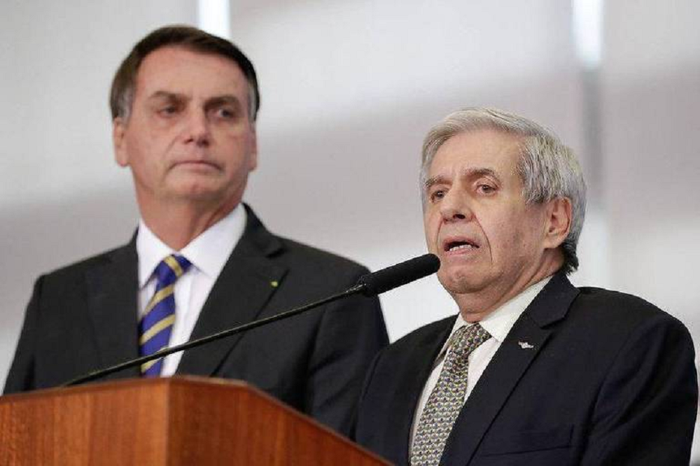 Jair Bolsonaro e general Augusto Heleno sérios, lado a lado, o segundo falando em microfone