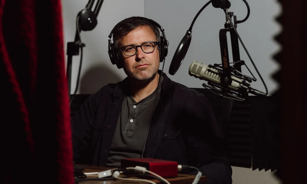 Daniel Denvir sério, em meio a microfones
