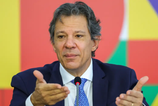 O ministro da Fazenda, Fernando Haddad, falando e gesticulando sem olhar para a câmera, sério