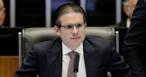 O presidente da Câmara, Hugo Motta, sério, de óculos, sentado, sem olhar para a câmera