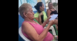 Idosa no centro de montagem, sentada, de camiseta cor de rosa, olhando papel, séria, de perfil