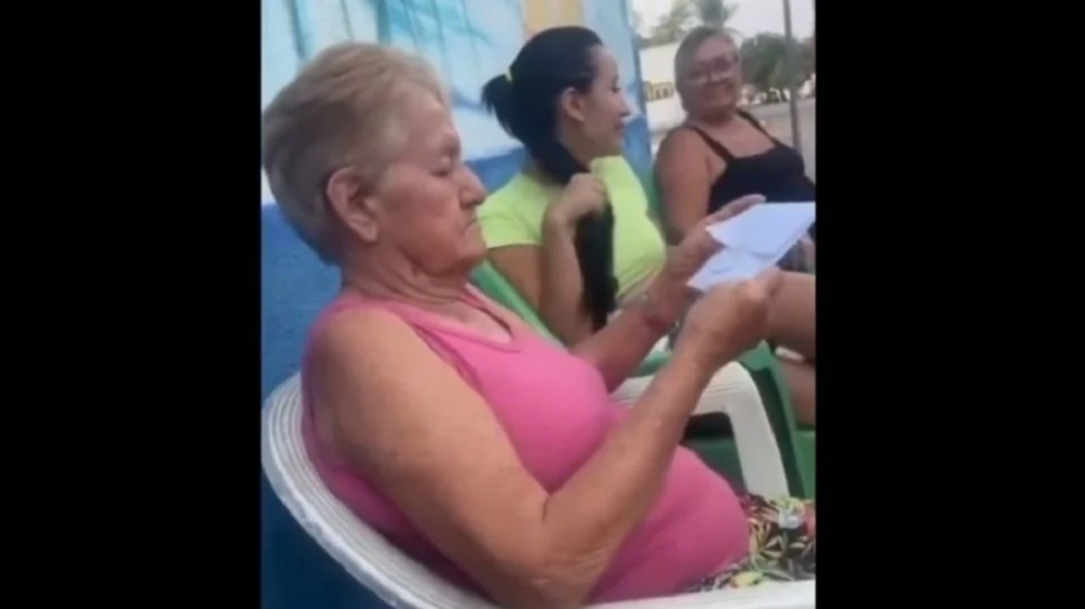 Idosa no centro de montagem, sentada, de camiseta cor de rosa, olhando papel, séria, de perfil