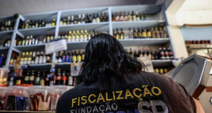 Agente fiscaliza bebidas em estabelecimento em São Paulo, de costas, com garrafas no fundo da foto