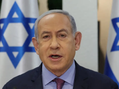 Benjamin Netanyahu falando, sério, com bandeiras de Israel ao fundo